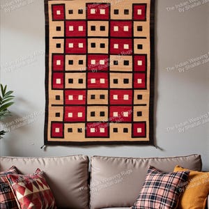 Può includere: Un arazzo da parete rettangolare tessuto con un motivo geometrico. Il design presenta quadrati alternati di rosso, beige, nero e bianco. Il tappeto è appeso a una parete grigia sopra un divano con cuscini decorativi. Il testo "Indian Weaving Rugs By Shaifali Jain" è stampato sull'immagine.