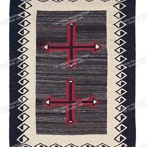 Op de afbeelding: Rechthoekig geweven vloerkleed met een donkerblauwe rand en een crèmekleurige binnenrand. Het midden heeft een donkergrijs veld met twee rode kruisen met pijlvormige uiteinden. Het vloerkleed heeft een geometrisch ruitpatroon.