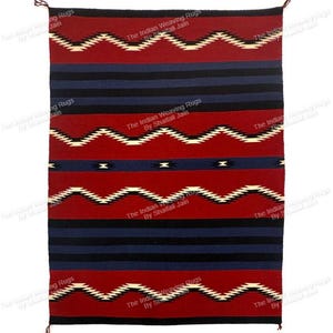 Puede incluir: Una alfombra rectangular tejida con un patrón geométrico. La alfombra presenta bandas alternas de rojo, azul marino y negro. Patrones en zigzag blancos y negros acentúan las secciones rojas. Se ven borlas en los bordes superior e inferior.