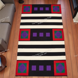 Può includere: Un tappeto rettangolare con un design geometrico nero, bianco e rosso. Il tappeto presenta strisce nere, quadrati rossi e verdi con motivi a rombi viola e quadrati viola. Il testo "The Indian Weaving Rugs Shaifali Jain" è stampato sul tappeto.