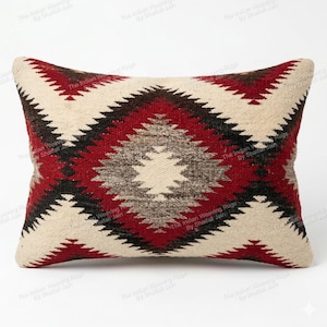 Puede incluir: Cojín decorativo rectangular con un patrón geométrico de diamantes en rojo, negro y crema. El cojín tejido presenta un diseño central de diamante, adecuado para la decoración del hogar. Aproximadamente 60 cm de largo.