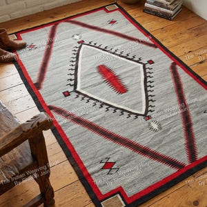 Pode incluir: Tapete retangular cinza com um design geométrico com detalhes em vermelho e preto. O tapete tem uma forma de diamante central com um design vermelho e é delimitado por uma borda preta e vermelha. O texto "The Indian Weaving Rugs By Shaifali Jain" está impresso no tapete.