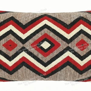 Puede incluir: Cojín rectangular decorativo con un patrón geométrico en rojo, negro y blanco sobre un fondo neutro. El cojín tiene un aspecto texturizado, lo que sugiere un diseño tejido o bordado. El patrón es simétrico.