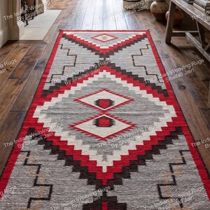 Puede incluir: Una alfombra rectangular con un patrón geométrico en tonos grises, rojos y negros. La alfombra presenta diseños de diamantes y zigzags, creando una estética del suroeste o tribal. Está colocada sobre un suelo de madera.