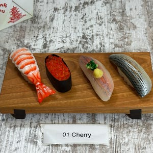 May include: A wooden sushi serving board with four pieces of nigiri sushi. The sushi includes shrimp, roe, and fish. A white label with "01 Cherry" is in the foreground. A Chinese takeout box is in the background.