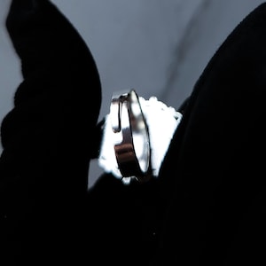 May include: A silver ring with a bright, reflective surface. The ring is set against a dark background, highlighting its metallic shine. The ring's design is simple and elegant, suitable for everyday wear.