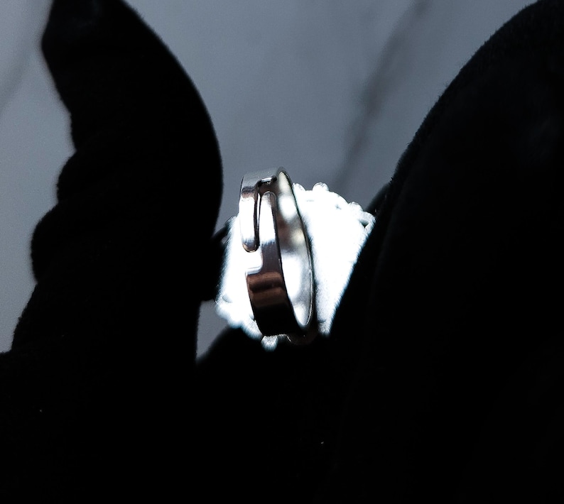 May include: A silver ring with a bright, reflective surface. The ring is set against a dark background, highlighting its metallic shine. The ring's design is simple and elegant, suitable for everyday wear.