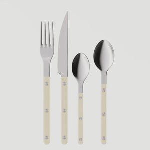 May include: A four-piece stainless steel flatware set. The set includes a fork, knife, teaspoon, and tablespoon. Each piece has a cream-colored handle with three silver rivets. The knife has a serrated blade.