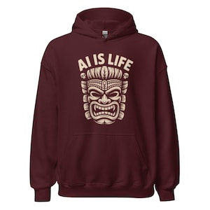 May include: A maroon hoodie with a cream Tiki mask design and the text "AI IS LIFE". The graphic includes skulls. The hoodie has a drawstring hood and a front pocket.