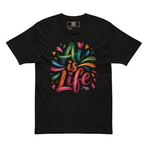 Może przedstawiać: Czarny t-shirt z napisem "Art is Life" w kolorowych, stylizowanych literach. Projekt zawiera serca i plamy w kolorze niebieskim, zielonym, pomarańczowym i różowym. Koszulka ma okrągły dekolt i krótkie rękawy.