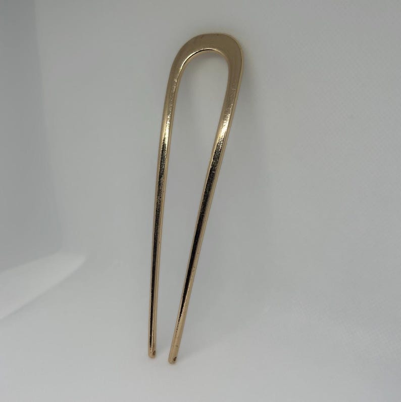 Peut inclure: Une &eacute;pingle &agrave; cheveux dor&eacute;e avec un dessus en forme de U et deux longues broches droites. L'accessoire pour cheveux est en m&eacute;tal et a une finition brillante. L'&eacute;pingle est con&ccedil;ue pour maintenir les cheveux en place.