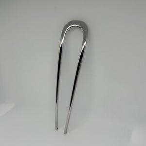 Peut inclure: Une &eacute;pingle &agrave; cheveux argent&eacute;e avec un dessus en forme de U et deux longues broches fines. L'&eacute;pingle a une surface polie et r&eacute;fl&eacute;chissante, con&ccedil;ue pour fixer les cheveux. L'accessoire pour cheveux est pr&eacute;sent&eacute; sur fond blanc.