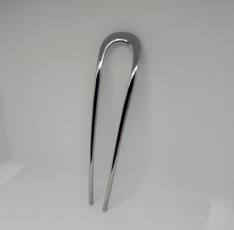 Peut inclure: Une &eacute;pingle &agrave; cheveux argent&eacute;e avec un dessus en forme de U et deux longues broches fines. L'&eacute;pingle a une surface polie et r&eacute;fl&eacute;chissante, con&ccedil;ue pour fixer les cheveux. L'accessoire pour cheveux est pr&eacute;sent&eacute; sur fond blanc.