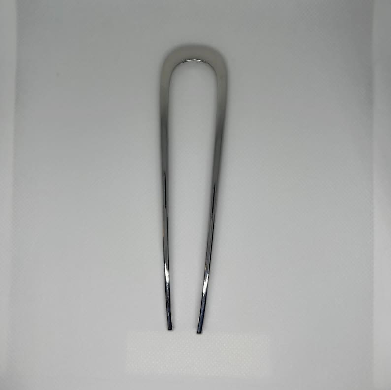 Peut inclure: Une &eacute;pingle &agrave; cheveux argent&eacute;e brillante en forme de U. L'&eacute;pingle est en m&eacute;tal lisse et r&eacute;fl&eacute;chissant, con&ccedil;ue pour maintenir les cheveux en place. L'&eacute;pingle est pr&eacute;sent&eacute;e sur un fond blanc.