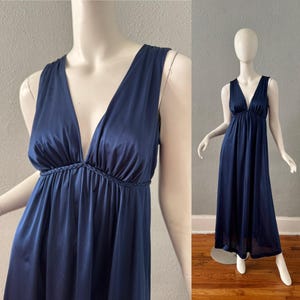 May include: A navy blue, floor-length gown with a deep V-neckline. The dress features a braided detail at the waist and wide straps. The dress is displayed on a mannequin.