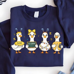 May include: Navy blue sweatshirt featuring four cartoon geese, each with a Pi-themed design. One goose holds a pie with "3.14", another holds a chalkboard with "π=3.14159", and the others have Pi symbols and accessories.