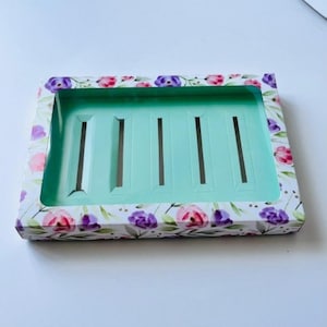 May include: Rectangular gift box with a floral pattern in pink and purple. The interior is a light teal color with vertical slots. The box is designed to hold multiple items, likely jewelry or small gifts.