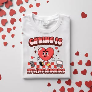 Könnte beinhalten: Weißes T-Shirt mit einem Grafikdesign, das ein rotes Herz-Zeichen mit einem lächelnden Gesicht zeigt, das einen Taschenrechner hält und auf einen Computer zugeht. Der Text lautet "C#DING IS MY LOVE LANGUAGE" in einer Retro-Schriftart. Rote Herzkonfetti umgeben das Shirt.