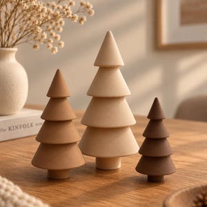 Op de afbeelding: Drie kegelvormige boombeeldjes in verschillende tinten bruin, beige en crème. Elke boom heeft een gelaagd ontwerp met een gladde, matte afwerking en een kleine cilindrische voet, samen opgesteld op een houten oppervlak.