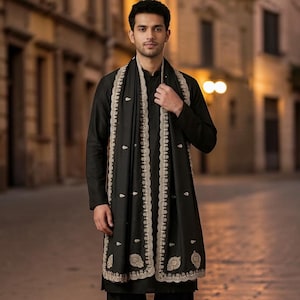 May include: A black long-sleeved kurta with matching trousers and a black shawl featuring intricate beige embroidery along the edges and scattered floral motifs. The shawl is draped over the shoulders, complementing the solid black ensemble.