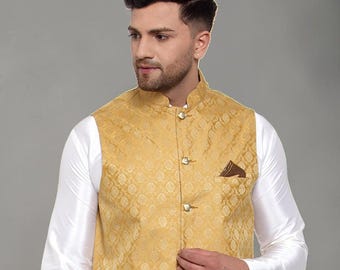 May include: A gold-colored sleeveless vest featuring a subtle repeating diamond pattern, a mandarin collar, and four metallic buttons down the front. A small dark brown pocket square is tucked into the left chest pocket over a white shirt.