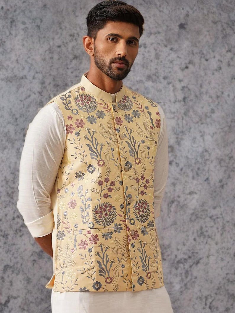 May include: A sleeveless vest in a pale yellow hue featuring a detailed floral pattern in shades of blue, red, and grey. The garment has a mandarin collar, a front button closure with metallic buttons, and two lower pockets on the front panel.