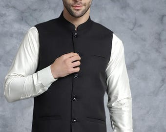 May include: A black Nehru-collared vest with four buttons and two pockets, worn over a white long-sleeve shirt. The vest is tailored and appears to be made of a smooth fabric. The background is a mottled gray.