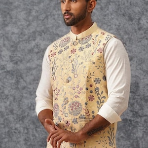 May include: A light yellow sleeveless vest featuring a mandarin collar and a button-down front. The garment is decorated with an intricate floral pattern in shades of blue, pink, and grey. It is worn over a plain white long-sleeved shirt.