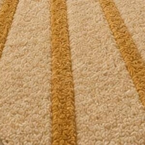 May include: A rectangular area rug featuring a textured, high-pile surface with alternating diagonal stripes in cream and mustard yellow. The rug has a thick, tufted construction that creates a distinct pattern of radiating lines across the fabric.