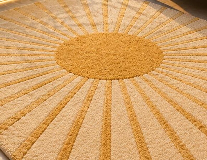May include: A circular rug featuring a central mustard yellow circle with a textured surface, surrounded by alternating radiating rays of mustard yellow and cream white. The entire design has a consistent, dense, and tufted pile texture throughout.