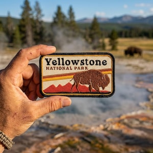 May include: Rectangular patch with the text "Yellowstone National Park" above a brown bison graphic. The patch has a black border and a background of red, orange, and yellow stripes.