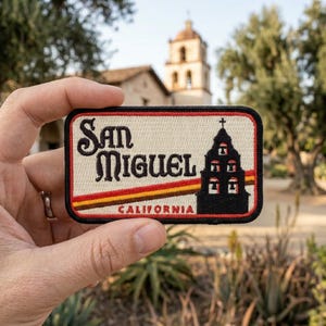 May include: A rectangular patch with the text "San Miguel California" in black and brown lettering. The patch features a church silhouette and a striped design in red, yellow, and brown.