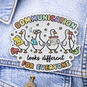 May include: Embroidered patch featuring four cartoon geese, each holding different communication tools. The patch reads "COMMUNICATION looks different FOR EVERYONE" in colorful text, sewn onto a denim jacket.