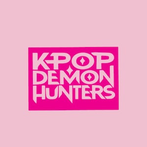 Può includere: Una grafica rosa con le parole "KPOP DEMON HUNTERS" in bianco, con un font stilizzato. Il testo è all'interno di un rettangolo rosa, su uno sfondo rosa chiaro. Il design presenta forme a diamante.