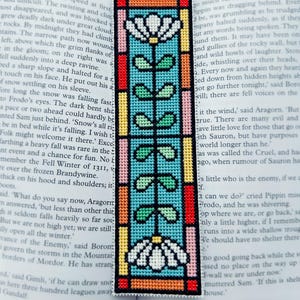 Könnte beinhalten: Handgefertigter Lesezeichen mit einem Buntglasdesign. Das Lesezeichen zeigt ein zentrales türkisfarbenes Feld mit einem floralen Stielmuster, umrahmt von farbenfrohen Rändern in Rot, Rosa, Gelb und Orange. Das Lesezeichen ist rechteckig.
