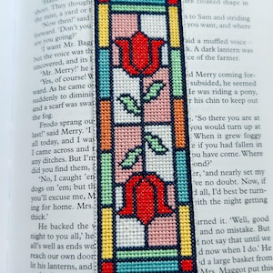 Op de afbeelding: Geborduurd boekenlegger met een tulpontwerp in glas-in-loodstijl. De boekenlegger heeft rode tulpen, groene bladeren en stelen, omlijst door kleurrijke randen. Perfect voor boekenliefhebbers.