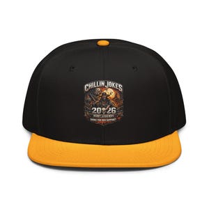 以下が含まれることがあります： 黒と黄色のフラットブリム野球帽。前面に「CHILLIN JOKES」と「20 26 HUNT LEGENDS DANKE FUR DEN SUPPORT！」の文字が入ったグラフィックが特徴です。帽子は黄色のつばとボタン、黒いクラウンが付いています。
