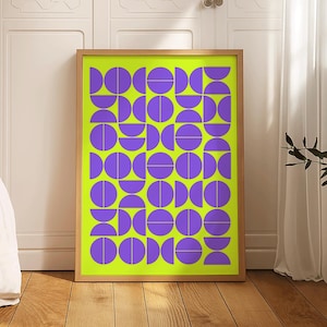 May include: A framed art print featuring a geometric design. The artwork has a bright neon green background with a pattern of purple semi-circles and circles. The frame is a light brown color, and the print is displayed on a wooden floor.