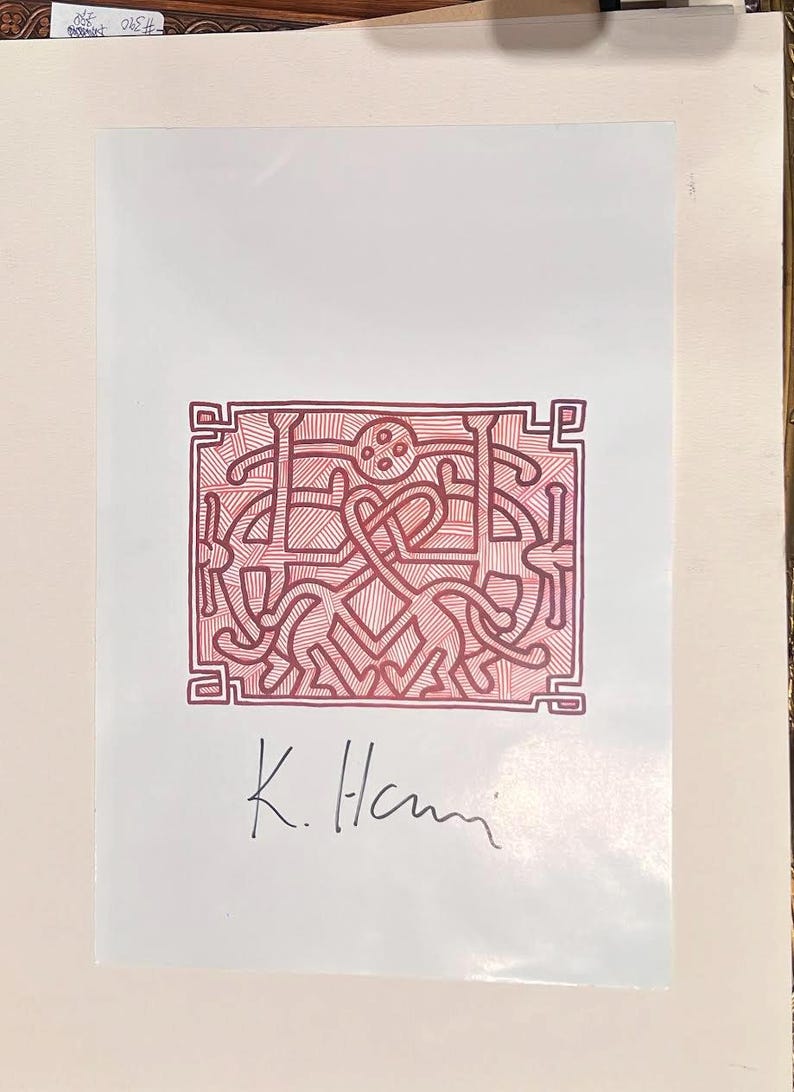 May include: A red and white print featuring a stylized design with interconnected figures and shapes within a rectangular border. The artwork is signed "K. Hani" in black ink. The print is on white paper.