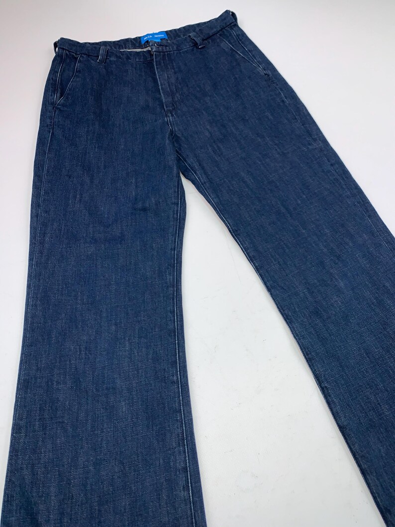 May include: Dark blue denim pants with a classic five-pocket design. The pants have a straight leg and a button and zipper closure. The waistline features belt loops. The pants are made of a sturdy denim material.