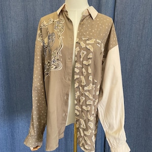 May include: A button-down shirt with a unique design. The shirt features a mix of patterns and colors, including a tan base with white and blue floral and abstract designs. One sleeve is solid white.
