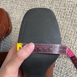 May include: Close-up of a brown patent leather shoe with a black sole. A pink measuring tape shows the shoe's width. The shoe size is 37. The sole is marked "pesie Veneziane".