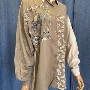 May include: A tan button-down shirt with a light beige collar and sleeves. The shirt features an elephant design with floral accents and a patterned panel. The sleeves are long and the shirt has a relaxed fit.