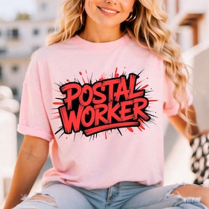 Può includere: T-shirt rosa chiaro con la scritta "POSTAL WORKER" in rosso, bordata di nero, con un design a spruzzi. La maglietta è a maniche corte e ha una vestibilità ampia.
