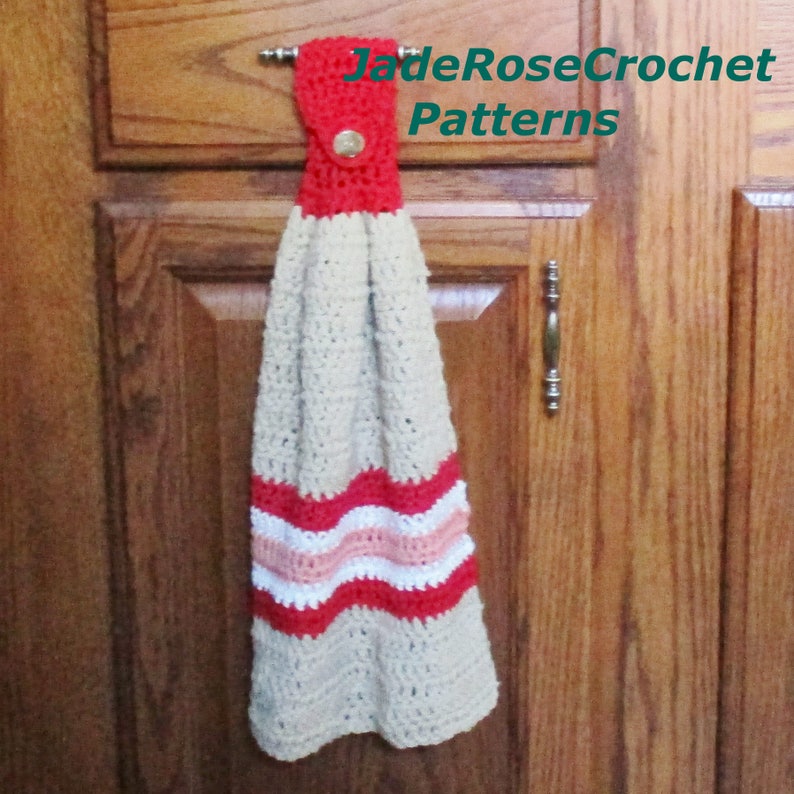 May include: A crocheted kitchen towel with a red, white and pink striped design. The towel is hanging on a wooden cabinet door with a metal hook. The text "JadeRoseCrochet Patterns" is visible in the top right corner of the image.
