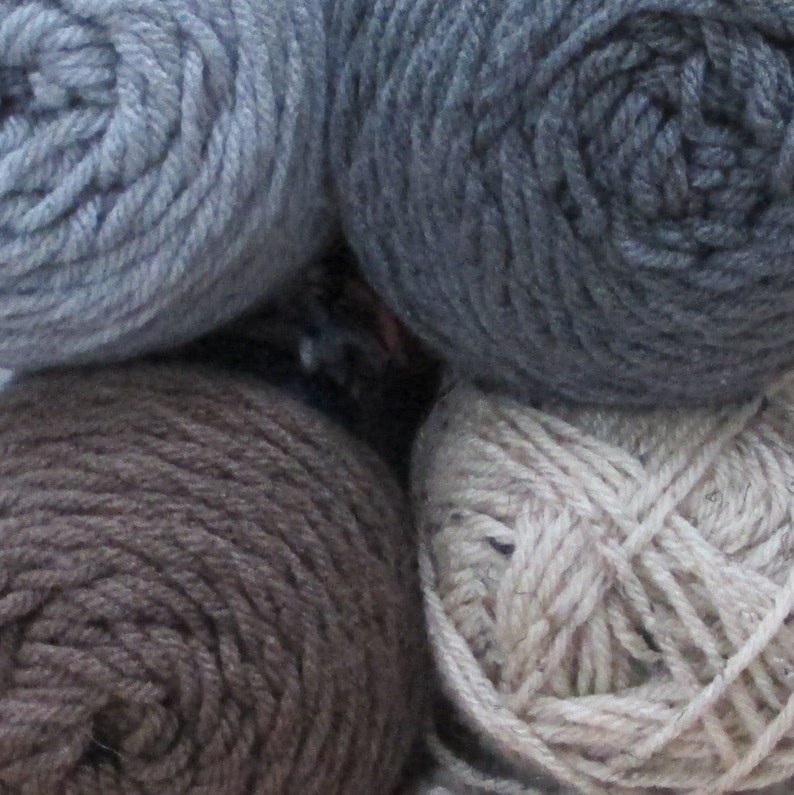 Pode incluir: Quatro novelos de l&atilde; em diferentes tons de azul, marrom e bege. A l&atilde; est&aacute; enrolada em novelos e pronta para ser tricotada ou crochetada.