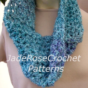 May include: A crocheted cowl in shades of blue and purple. The cowl is made with a textured stitch and has a loose, drapey fit. The text "JadeRoseCrochet Patterns" is visible on the cowl.