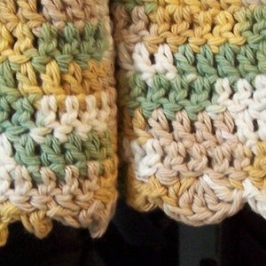 May include: Close-up of a crocheted dishcloth with a scalloped edge. The dishcloth is made with a multi-coloured yarn in shades of green, white, beige, and yellow.