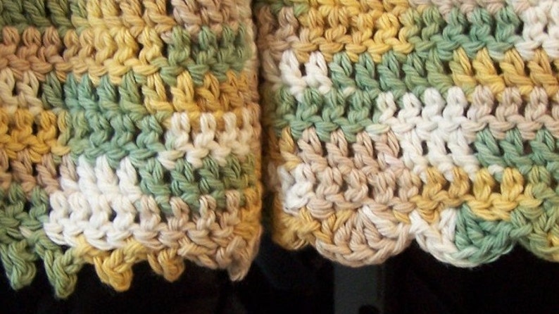 May include: Close-up of a crocheted dishcloth with a scalloped edge. The dishcloth is made with a multi-coloured yarn in shades of green, white, beige, and yellow.