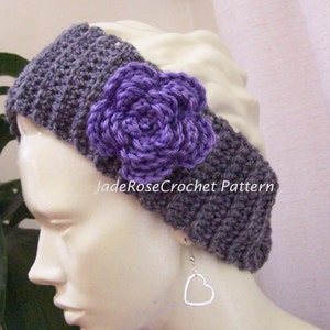 Könnte beinhalten: Gehäkeltes Stirnband in Grau mit einer lila Blume. Das Stirnband hat eine große, lila gehäkelte Blume. Der Text "JadeRoseCrochet Pattern" ist sichtbar. Ein herzförmiger Silberohrring ist ebenfalls zu sehen.